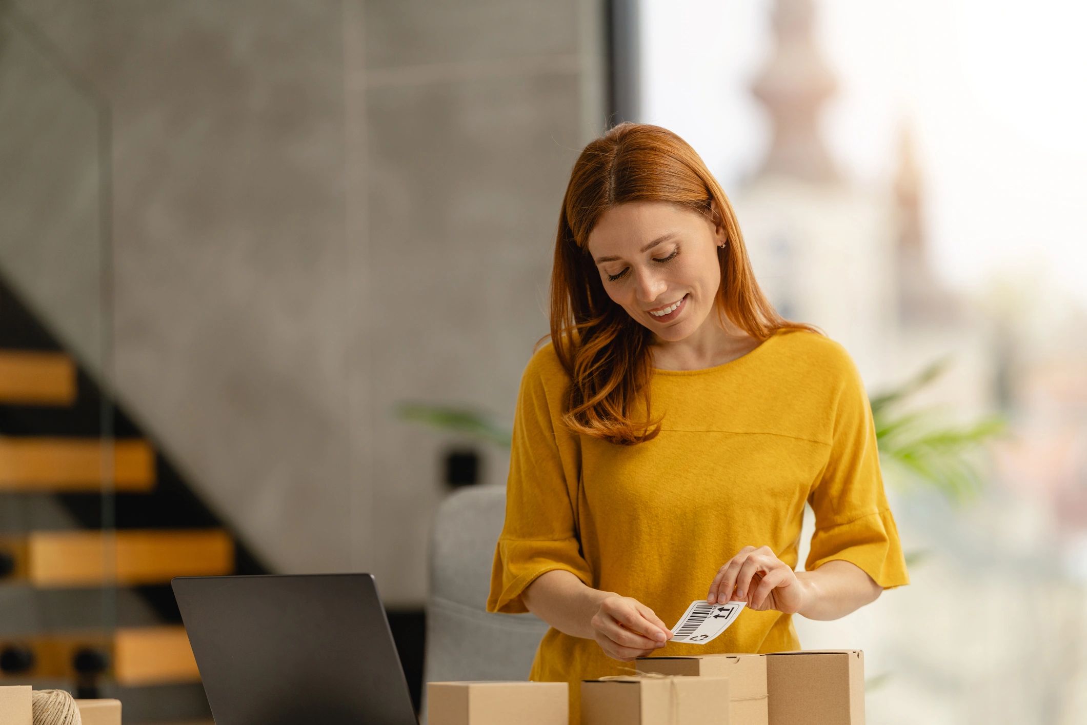 Entrepreneur packaging orders at home office with laptop and shipping labels