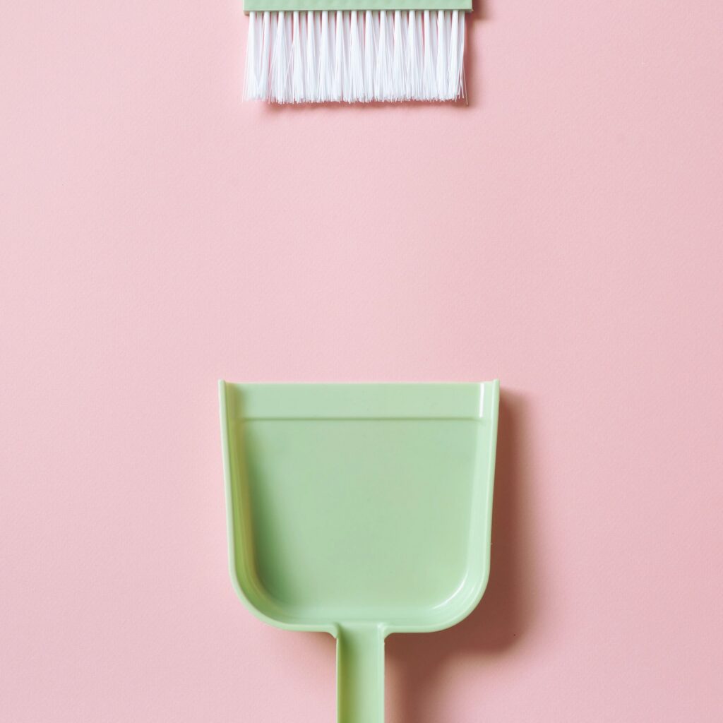 Green broom and dustpan isolated on pink background. top view, copy space