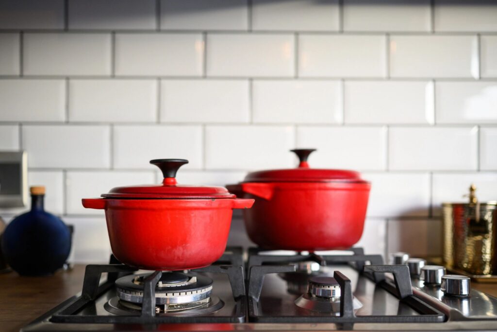 Closeup of two red enamel cast iron pots sitting on a gas stovetop in a modern kitchen